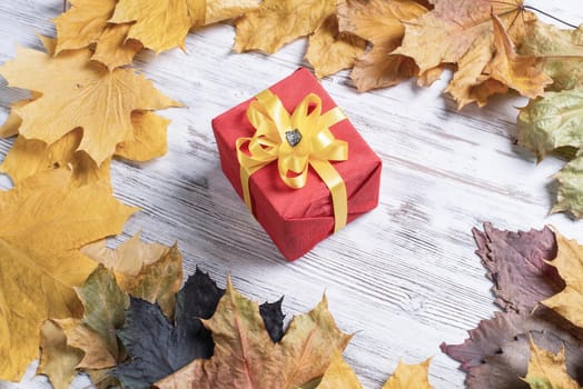 Bright autumn composition with gift box and yellow maple leaves. Holiday present decorated yellow ribbon bow lies on vintage wooden desk. Happy thanksgiving congratulation. Autumn sale advertising.