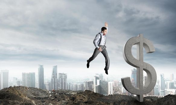 Jumping businessman in smart casual wear crashing big dollar symbol with city view on background.