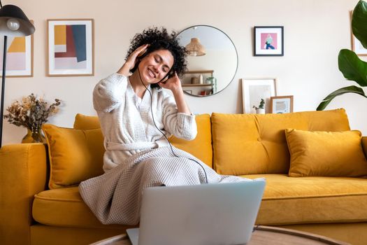 Happy young African American woman dancing at home living room relaxing listening to music with headphones. Copy space. Lifestyle concept.