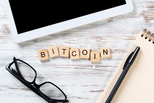 Bitcoin cryptocurrency concept with letters on cubes. Blockchain and digital money. Still life of workplace with supplies. Flat lay vintage wooden desk with tablet computer and spiral notebook.