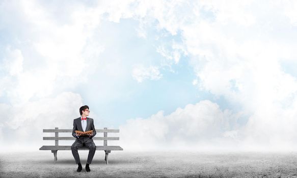 Student sits on a bench, holding a book. Traditional education concept