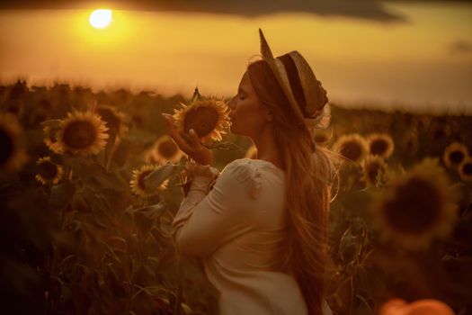 Beautiful middle aged woman looks good in a hat enjoying nature in a field of sunflowers at sunset. Summer. Attractive brunette with long healthy hair