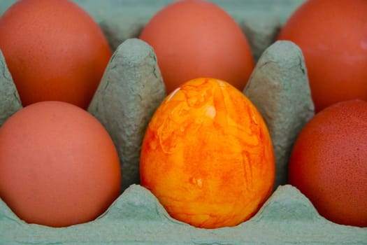 In the cardboard package yellow eggs. One egg differs in color from the others