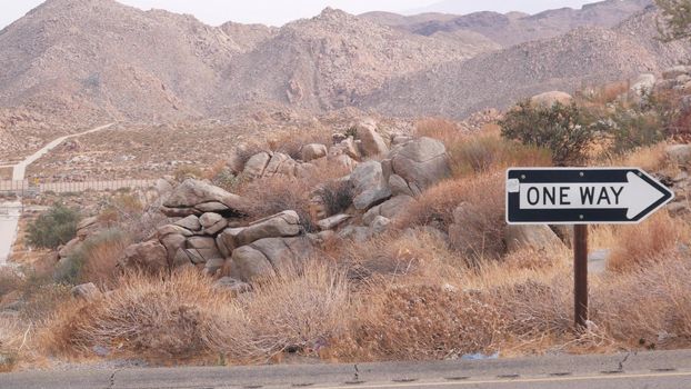 One way road transport sign with arrow on roadside or wayside, highway or freeway in California USA. Road trip in desert valley among mountains and hills with boulders. Western wilderness nature.