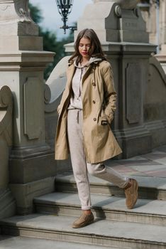 Portrait of fashionable women in beige sports suit, trench coat and stylish suede loafer posing on the stone stairs. street look fashion