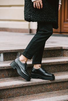 Fashion photo of young woman in black fur coat, jeanse and shoes at city street