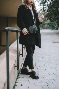 Fashion photo of young woman in black fur coat, jeanse and shoes at city street. beige jacket with a hood