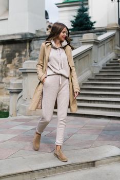 Portrait of fashionable women in beige sports suit, trench coat and stylish suede loafer posing on the stone stairs. street look fashion