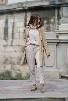 Portrait of fashionable women in beige sports suit, trench coat and stylish suede loafer posing on the stone stairs. street look fashion
