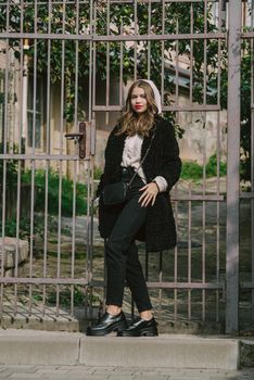 Fashion photo of young woman in black fur coat, jeanse and shoes at city street. beige jacket with a hood