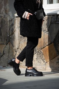 Fashion photo of young gorgeous beautiful woman in black fur coat, jeanse and shoes at city street