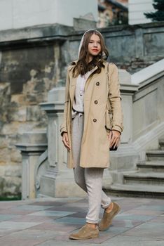 Portrait of fashionable women in beige sports suit, trench coat and stylish suede loafer posing on the stone stairs. street look fashion