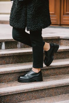 Fashion photo of young woman in black fur coat, jeanse and shoes at city street