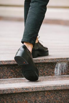 Fashion photo of young woman in black fur coat, jeanse and shoes at city street