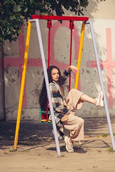 Closeup portrait of young beautiful fashionable woman wearing checkered long coat, beige pants and white blouse . Lady posing on city building background. Female fashion.