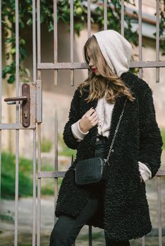 Fashion photo of young woman in black fur coat, jeanse and shoes at city street. beige jacket with a hood
