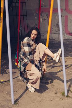 Closeup portrait of young beautiful fashionable woman wearing checkered long coat, beige pants and white blouse . Lady posing on city building background. Female fashion.