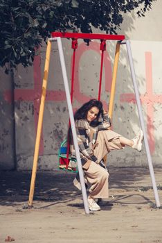 Closeup portrait of young beautiful fashionable woman wearing checkered long coat, beige pants and white blouse . Lady posing on city building background. Female fashion.