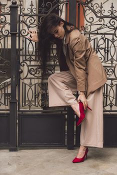 Close up portrait of young beautiful woman with long brunette curly hair posing against building background. woman wearing a white blouse and beige pants and a jacket