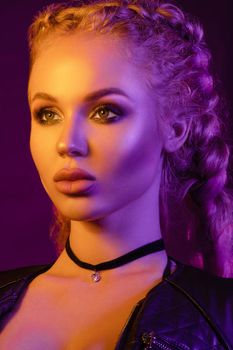 Fashion portrait of stunning sexy young blonde woman with trendy braids and sparkling bra under the net top. She is holding peace sign by the eye, making pouting lips in bright pink and yellow light.