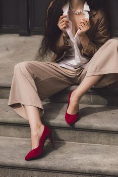 Close up portrait of young beautiful woman with long brunette curly hair posing against building background. woman wearing a white blouse and beige pants and a jacket