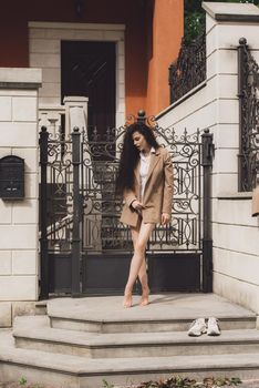 Close up portrait of young beautiful woman with long brunette curly hair posing against building background. woman wearing a white blouse and beige jacket