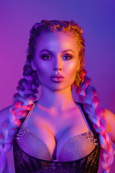 Fashion portrait of stunning sexy young blonde woman with trendy braids and sparkling bra under the net top. She is holding peace sign by the eye, making pouting lips in bright blue and red light.