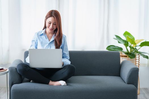 Woman enjoy with content streaming movies or social media application on laptop computer sitting on sofa at home