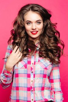 Studio portrait of stunning beauty with gorgeous brunette wavy hair with red lips in colorful plaid shirt looking at camera with smile over pink background. Isolate.