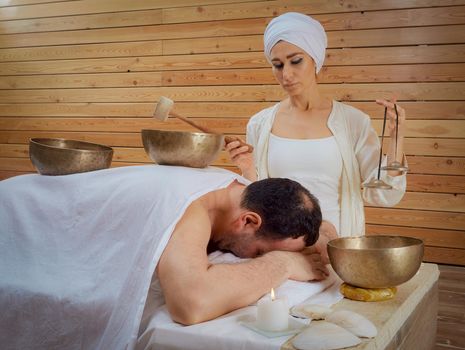 The woman is treated with Tibetan singing bowls and bells, while the man lies under a white sheet. Relaxing meditation.