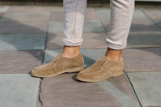 Portrait of fashionable women in beige pants and stylish suede loafer shoes posing in the street. Stone tiles