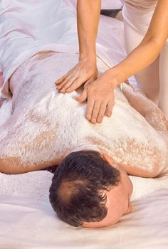 A woman healer performs a ritual with salt, rubs the back of a lying man with salt. Relaxation.