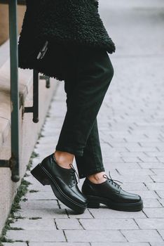 Fashion photo of young woman in black fur coat, jeanse and shoes at city street