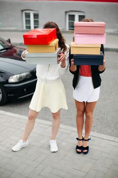 Unrecognizable girlfriends holding boxes of shoes standing in the street.