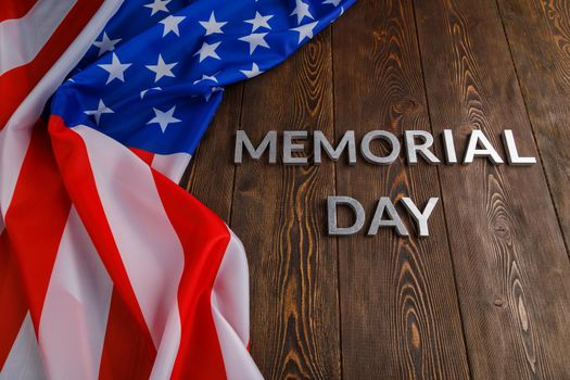 the words memorial day laid with silver metal letters on wooden board surface with crumpled usa flag.