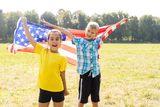 Happy Caucasian girl and boy smiling laughing holding hands and waving American flag outside celebrating 4th july, Independence Day, Flag Day concept