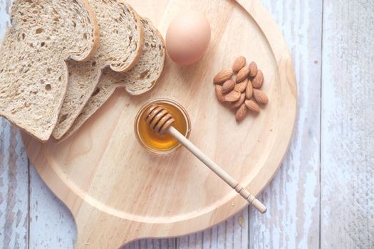Top view of fresh honey , bread , egg and almond nut on table .