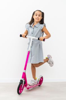 Adorable little girl using a scooter. Isolated on white background.