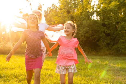 Patriotic holiday. Happy family, mother and daughters with American flag outdoors on sunset. USA celebrate independence day 4th of July