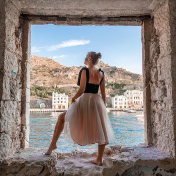 Side view portrait of a relaxed woman breathing fresh air at the seaside. She stands on the window in the old building