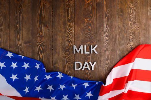 the word MLK day laid with silver metal letters on wooden surface with crumpled USA flag at lower side in directly above high angle view. MLK means Martin Luther King Jr.