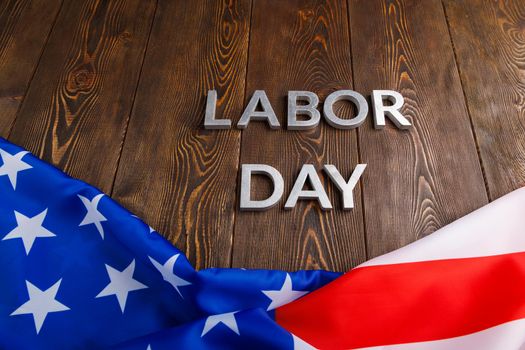 words labor day laid with silver metal letters on wooden surface with crumpled USA flag on bottom side in linear perspective view