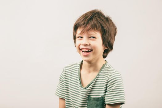 Happy six year old Caucasian boy portrait over grey background. White European kid widely smiling and looking into the camera