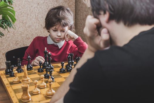 Thoughtful six years old boy playing chess with his father pondering on making move. Leisure activities during quarantine