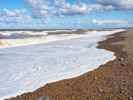 Rolling waves crash onto the beach under blue sky and white clouds, Blakeney Point, Cley next the Sea, Norfolk, UK