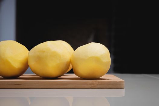 Close-up Several peeled potatoes on a wooden cutting board on a white table