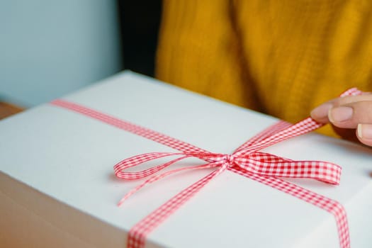 Girl's fingers hold red checkered ribbon on gift box. Holiday mood. Festive surprise for Christmas, New Year or Birthday.