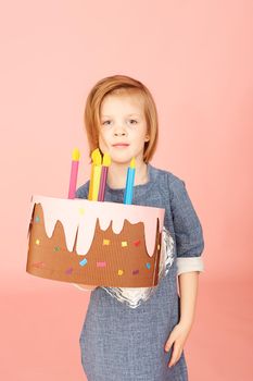 Portrait of an excited pretty little girl celebrating birthday and showing cake on over pink background