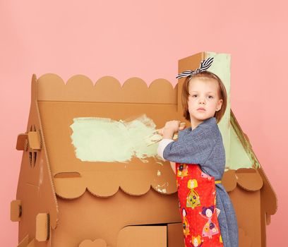 Young Girl Painting Big Cardboard House on over pink background.