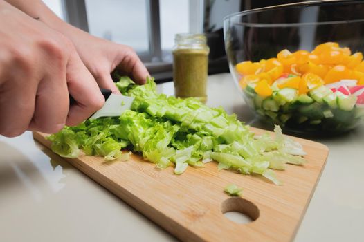Close-up of a girl's hand cut a salad on a wooden table, a woman prepares a vegetarian salad, healthy food, a knife cuts greens.